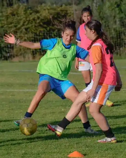 Drei Spielerinnen trainieren gemeinsam auf einem Fußballplatz.